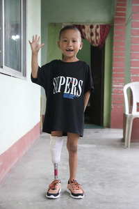 Young boy standing tall on his new prosthesis, waiving and smiling to the photographer