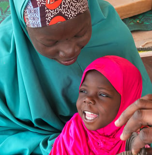 Massalouka, a young girl wearing pink head covering, and her mother, Manssoura wearing a teal head covering, both smile. © J. Labeur / HI