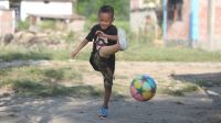 Young boy with prosthetic leg in full motion, mid-kicking a rainbow soccer ball