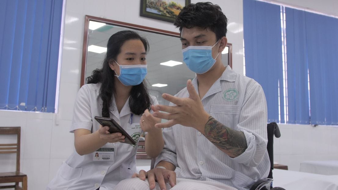 A rehabilitation professional shows a patient how to use the OpenTeleRehab mobile app in Vietnam. 