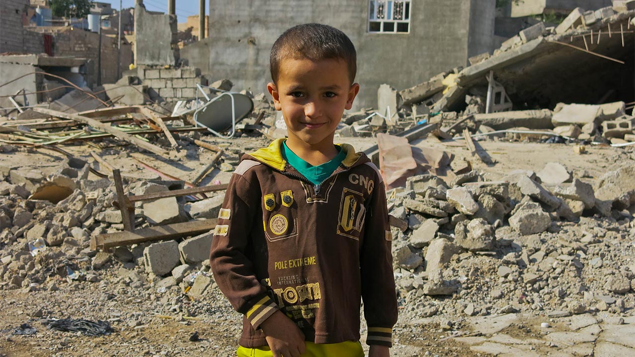 A child stands in front of damaged buildings in Jalawla, Iraq.
